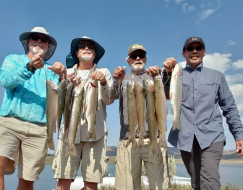 Four people holding up freshly caught fish, smiling against a blue sky with clouds.