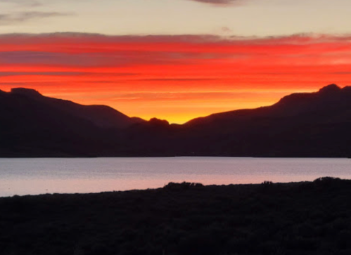 Vibrant sunset over a lake, with silhouetted mountains and colorful clouds reflecting on the water.