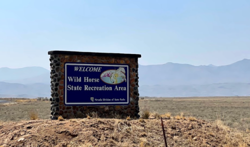 Welcome sign for Wild Horse State Recreation Area, with mountains in the background and a clear blue sky.