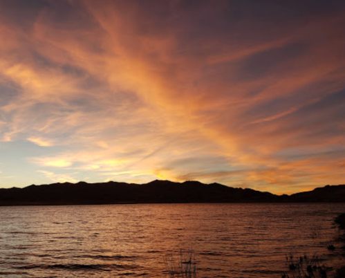A serene sunset over a calm lake, with colorful clouds reflecting on the water and mountains in the background.