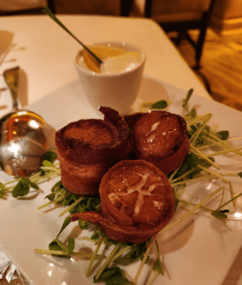 Three crispy, golden-brown rolls on a bed of greens, served with a small cup of dipping sauce.