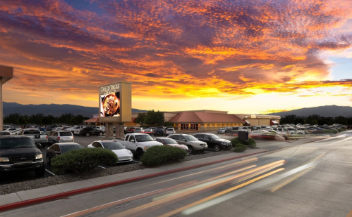 A busy parking lot at sunset, with a restaurant and colorful sky in the background.