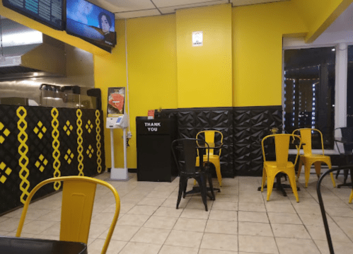 Interior of a bright yellow restaurant with black accents, featuring empty tables and a thank you sign.