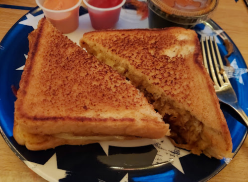 Grilled cheese sandwich cut in half, served on a star-patterned plate with dipping sauces on the side.