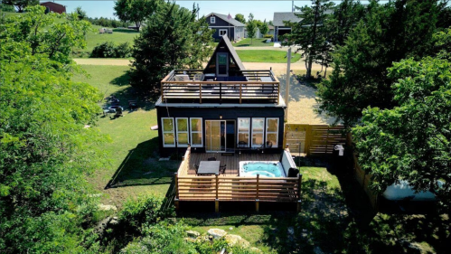 Aerial view of a modern house with a rooftop deck and hot tub, surrounded by greenery and open space.