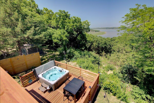 A hot tub on a wooden deck overlooking a lush landscape and a serene body of water in the distance.
