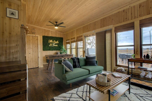 Cozy wooden living room with a green sofa, wooden accents, and large windows, featuring decorative plants and a modern vibe.