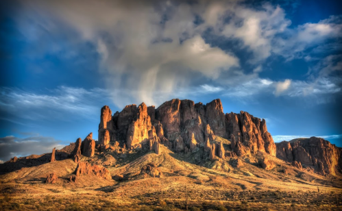 Majestic rock formation under a dramatic sky, with sunlight illuminating the rugged landscape.