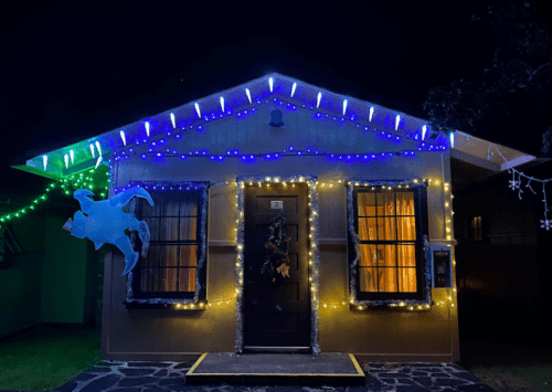 A cozy house decorated with colorful holiday lights, including blue and white icicle lights, glowing warmly at night.