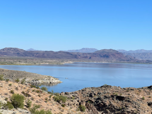 A serene landscape featuring a calm lake surrounded by rocky terrain and distant mountains under a clear blue sky.