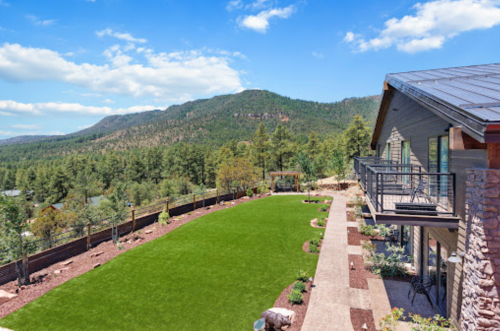A scenic view of a landscaped yard with green grass, stone pathways, and mountains in the background under a blue sky.