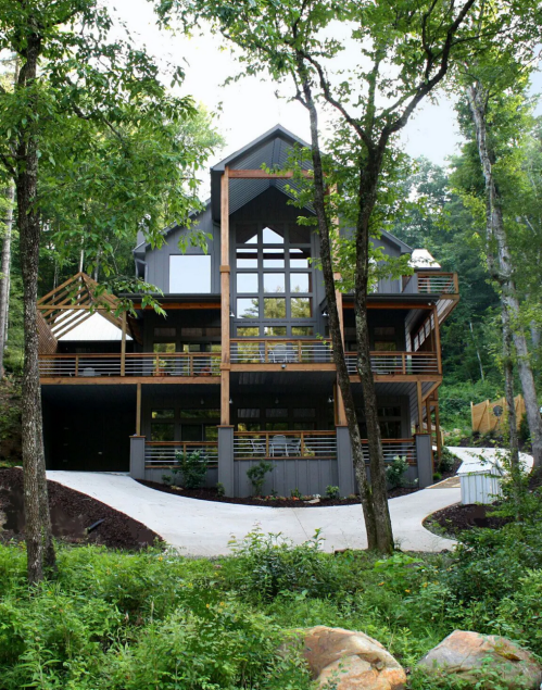 A modern house surrounded by trees, featuring large windows and multiple levels with a pathway leading up to it.
