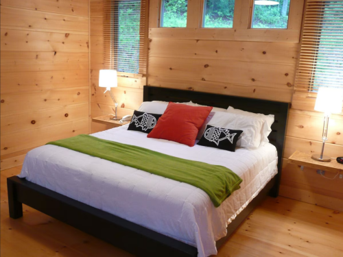 Cozy bedroom with a wooden interior, featuring a bed with green and red accents, and bedside lamps.