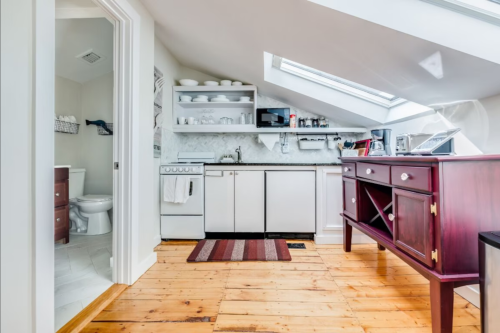 Bright attic kitchen with wooden floors, skylights, and modern appliances, featuring a dining table and a bathroom door.