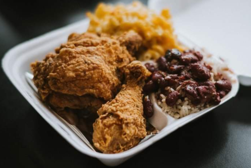 A takeout container with fried chicken, rice, red beans, and macaroni and cheese.