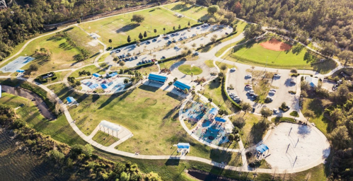 Aerial view of a park featuring sports fields, parking areas, and picnic spots surrounded by trees.