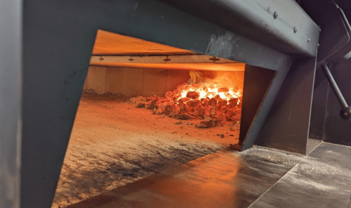 View of glowing coals inside a pizza oven, with a metal structure framing the opening.