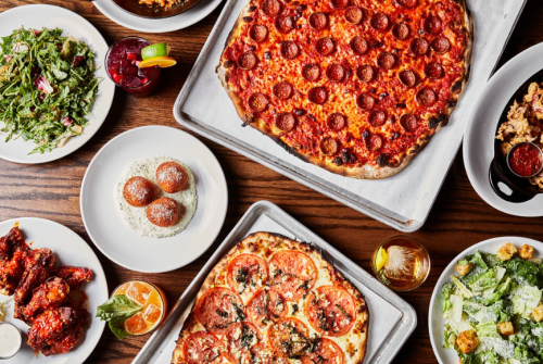A spread of delicious food including pepperoni pizza, salads, wings, and dessert on a wooden table.