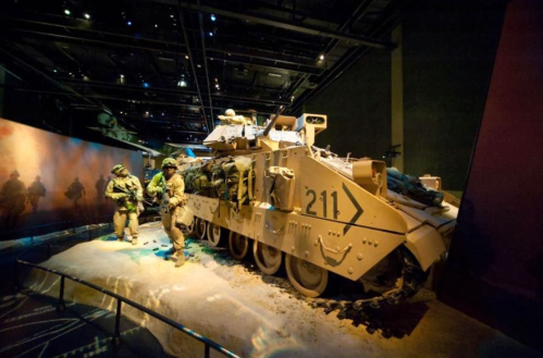 A military vehicle displayed in a museum, with soldiers in uniform standing nearby.