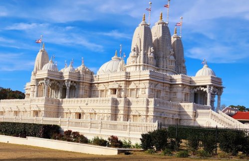 A stunning white marble temple with intricate carvings and domes, set against a blue sky.