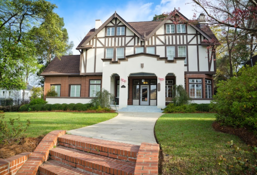 A charming two-story Tudor-style house with a brick pathway and lush green lawn.