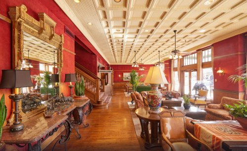 Elegant hotel lobby with red walls, ornate decor, wooden floors, and comfortable seating areas. Bright and inviting atmosphere.