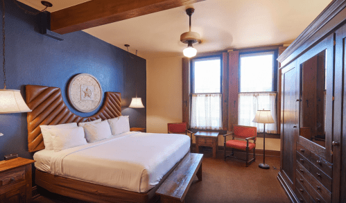 Cozy hotel room featuring a large bed, wooden furniture, and two windows with sheer curtains.