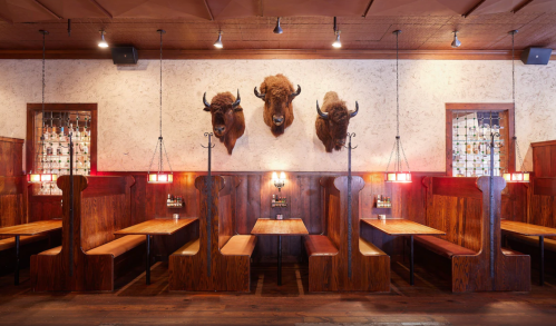 Rustic restaurant interior with wooden booths, dim lighting, and mounted bison heads on the wall.