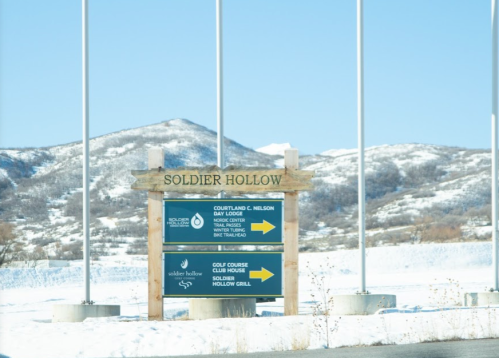 Sign for Soldier Hollow with directions to various facilities, set against a snowy mountain backdrop.