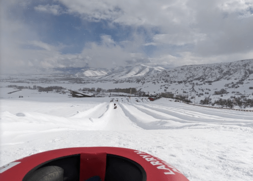 A snowy landscape with a view of a tubing hill and mountains in the background under a cloudy sky.