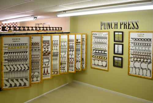 A wall display featuring various punch press designs and patterns in a workshop setting.