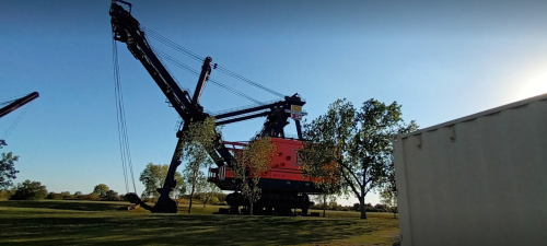 A large black and red crane stands in a park, surrounded by trees under a clear blue sky.