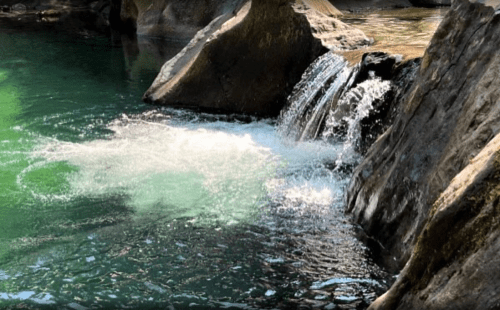 A serene waterfall cascading into a clear, greenish pool surrounded by rocky terrain.