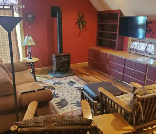 Cozy living room with a brown sofa, rocking chairs, a wood stove, and a TV against a red wall.