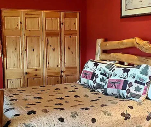 Cozy bedroom with a wooden bed, patterned quilt, and a red wall, featuring a wooden closet in the background.