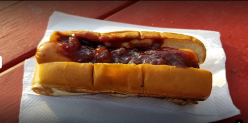 A hot dog in a bun topped with ketchup, resting on a napkin on a wooden surface.