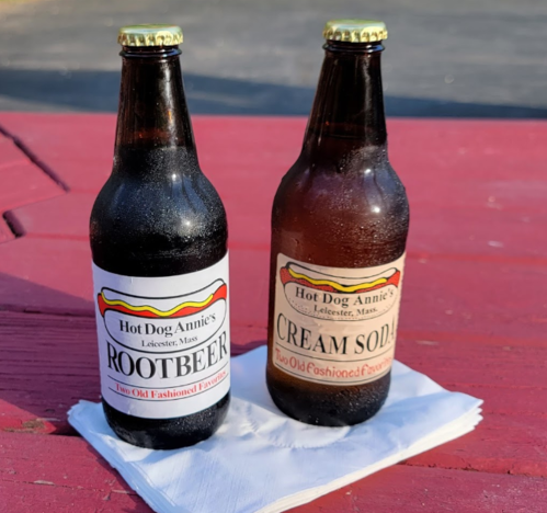 Two glass bottles of soda, labeled "Rootbeer" and "Cream Soda," on a red table with a napkin underneath.