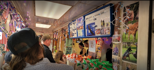 A busy food stall decorated with lights and photos, with customers waiting in line to order.