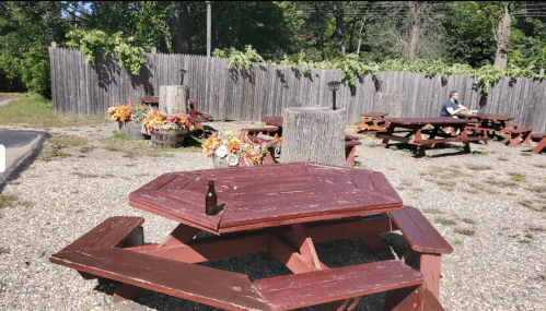 Outdoor seating area with picnic tables, surrounded by wooden fences and decorated with flowers and greenery.