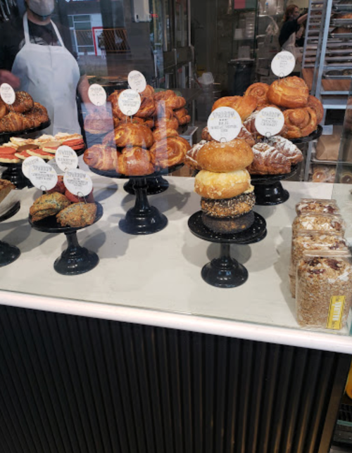 A display of various pastries on black stands, including croissants, donuts, and baked goods in a bakery setting.
