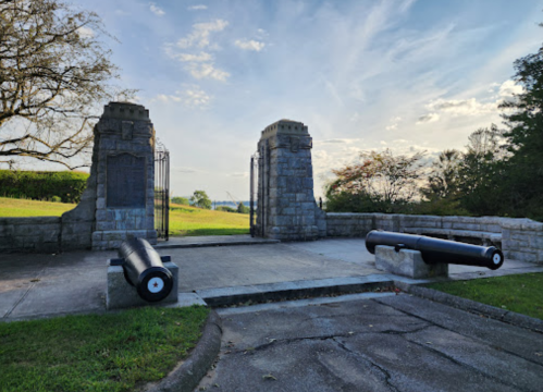 Stone gate with cannons on either side, set against a cloudy sky and green landscape.