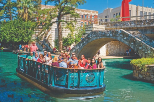 A group of people enjoying a boat ride on a scenic river, surrounded by greenery and historic buildings.