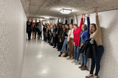 A group of people standing in a hallway, smiling and raising their arms in celebration.