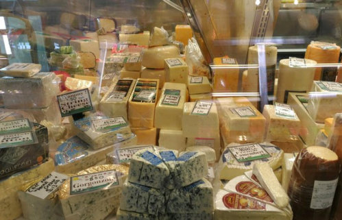 A variety of cheeses displayed in a glass case, each labeled with names and prices.