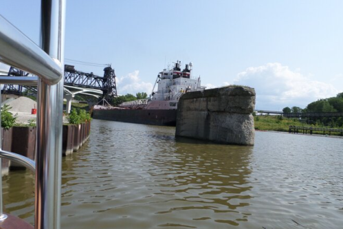 A tugboat navigates a canal near a large stone structure under a clear blue sky.