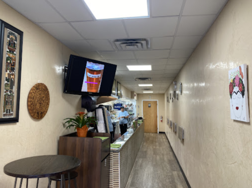 A narrow hallway in a cafe with a TV displaying a drink, a counter, and decorative wall art.