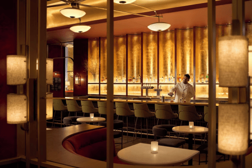 A bartender prepares drinks at a stylish bar with warm lighting and elegant decor.