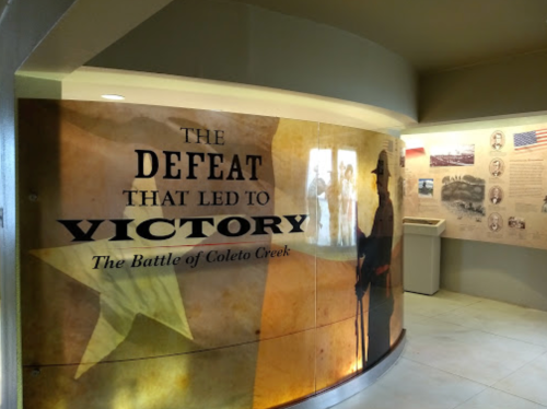 Exhibit display about the Battle of Coleto Creek, featuring text on defeat and victory with historical images.