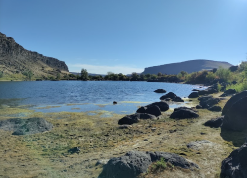A serene lake surrounded by rocky shores and hills under a clear blue sky.