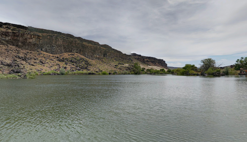 A calm river surrounded by rocky cliffs and sparse vegetation under a cloudy sky.